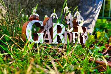 Kardamlalarının ve eski bir çinko küvetin önünde, fazla büyümüş çimlerin ortasında ahşap tabela..