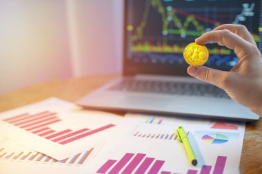 Masanın üzerinde Bitcoin laptop ve diyagramları önünde tutan el