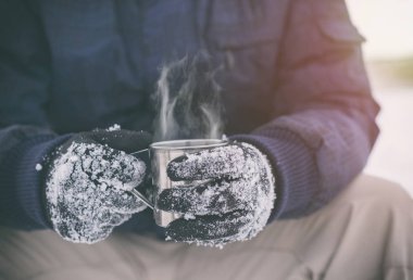 Fincan sıcak çay veya kahve ile tutarak eldiven erkek el yan görünüm. Çay molası. Kış zaman kavramı