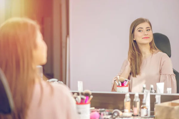 Woman in a beauty salon looks at her reflection in the mirror wi — Stock Photo, Image