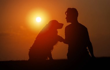 genç adam onun evcil köpek eğitim, dış ve bir yaz akşamı el sallayarak gökyüzünde güneşin tarafından kontrast oturuyor