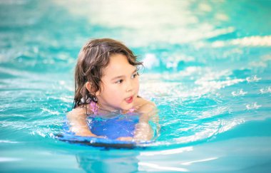 Gülümseyen kız yüzme havuzunda yüzen tahta ile eğleniyor