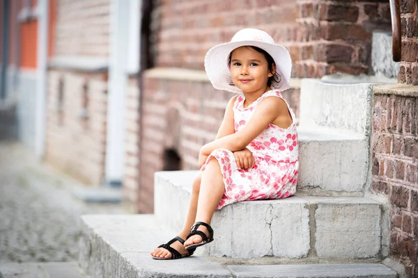 暖かく 日当たりの良い夏の日の階段に座っている白い帽子を身に着けている愛らしい少女 — ストック写真