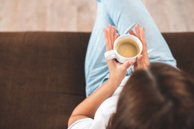 Kafkasyalı genç bir kadının kahve fincanı tutarken evdeki kanepede oturması.