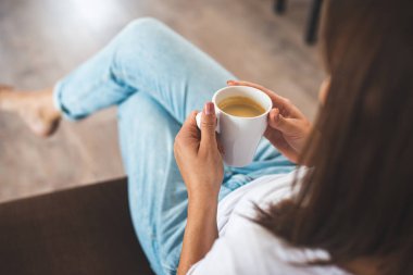 Kafkasyalı genç bir kadının kahve fincanı tutarken evdeki kanepede oturması.