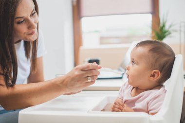 Anne küçük kızını kaşıkla besler.