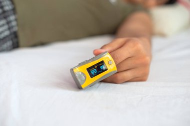 Kadının elinin yatakta dinlendiği yakın plan. Kan oksijeni doygunluğunu ölçmek için nabız oksimetresi takıyor.