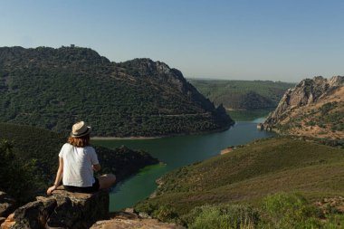 İspanya 'nın Monfrague kentindeki dağların arasından akan bir nehre tanıklık eden bir kayanın tepesinde oturan çekici genç kadın..