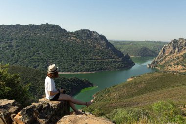 İspanya 'nın Monfrague kentindeki dağların arasından akan bir nehre tanıklık eden bir kayanın tepesinde oturan çekici genç kadın..