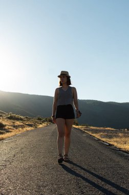 Çekici genç bir kadın, dağların ortasında şapkasıyla küçük bir yolda tek başına yürüyor.