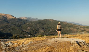Çekici genç bir kadın, İspanya, Extremadura 'nın kuzeyindeki manzaraya tanıklık ederken fotoğraf çekmek için refleks kamera takıyor.
