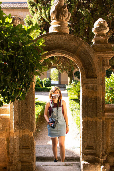 Привлекательная молодая женщина посещает старый монастырь в Испании в маске для лица и носит с собой рефлекторную камеру