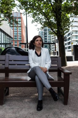 Beyaz takım elbiseli çekici genç bir kadın bankta oturup İngiltere 'deki ofisinde toplantıya başlamak için bekliyor.