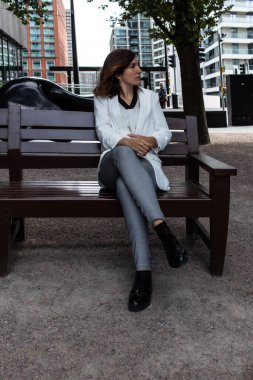 Beyaz takım elbiseli çekici genç bir kadın bankta oturup İngiltere 'deki ofisinde toplantıya başlamak için bekliyor.