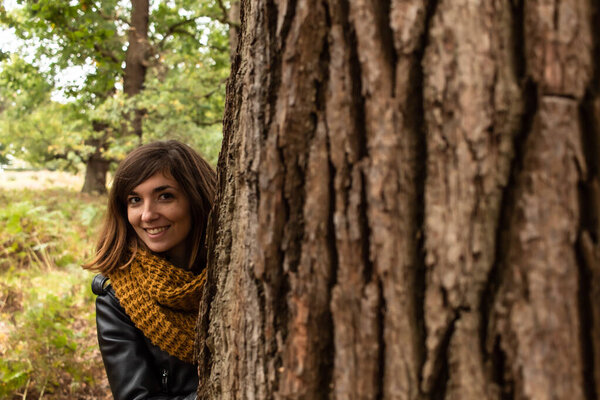 Детальная фотография привлекательной молодой женщины в черной кожаной куртке, расположенной рядом с стволом дуба