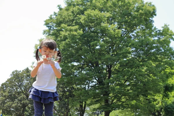 日本の女の子 歳のブルーの空の下でタンポポの種を吹く — ストック写真