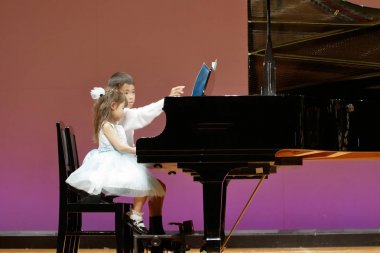 Japon kardeşi ve kız kardeşi sahnede piyano oynarken (9 yaşında çocuk ve 4 yaşında kız)