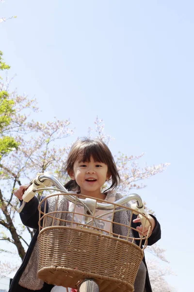 Chica japonesa montando en la bicicleta bajo flores de cerezo (4 años) ) — Foto de Stock