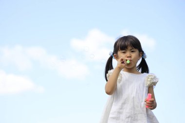 Japon kız mavi gökyüzünün altında baloncukla oynuyor (5 yaşında))