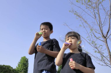 Japon erkek ve kız kardeş mavi gökyüzünün altında baloncukla oynuyorlar (10 yaşında oğlan ve 5 yaşında kız çocuğu))