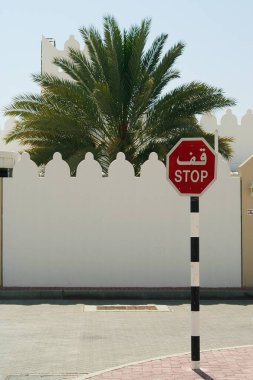 Isolated stop sign in front of white wall with battlements and palm tree, Oman clipart