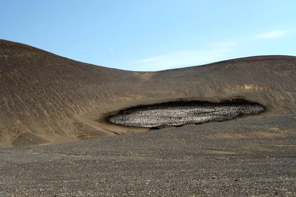 Barren dry landscape with spot of melted ice on black hill against blue sky, Iceland