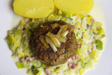 Pişmiş patates, köfte, soğan ve pırasa sebzeli beyaz tabakta görün.