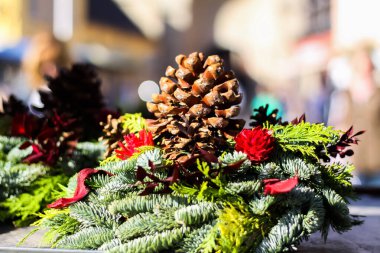 Kış Noel anlaşmasını çiçeklerle, köknar dallarıyla ve Alman pazarındaki parlak sonbahar güneşinde koni kozalaklarıyla kapatın. Şehir hayatının bulanık arka planı. Almanya.