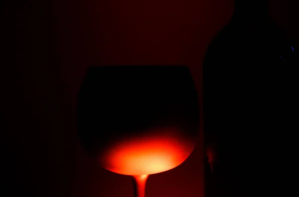 赤光沢のある光 黒の背景に照らされたシルエットの孤立したワイングラスとボトルのクローズアップ — ストック写真