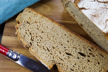 Taze Alman taş fırınından yapılmış ekmeği kapat, dilimle ve tahta kesme tahtasının üzerinde çıtır çıtır beyaz ekmek kes.