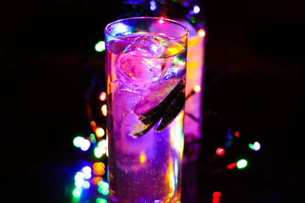 キュウリとジン強壮剤 ピンク紫色の氷のキューブとカクテルグラスを閉じます カラフルな鮮やかなボケの背景 — ストック写真
