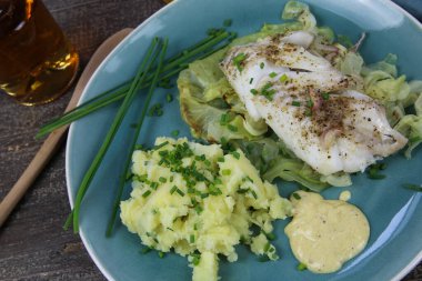 Sivri lahana, hardal sosu ve soğanlı patates püresi soslu morina filetosu ile izole edilmiş mavi porselen tabağı.