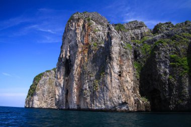 Tropikal ada Ko Phi Phi 'nin kıyı şeridi boyunca mavi gökyüzü altında etkileyici kaya oluşumları boyunca tekne gezisi.