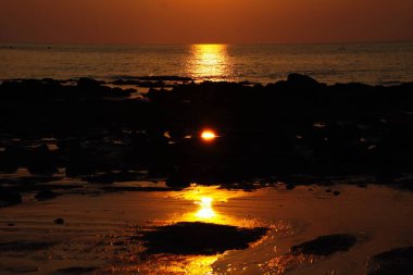 Gün batımında güneş ışığı okyanusun üzerine uzun sarı bir ışık demeti salıyor. Işın, alçak gelgit sırasında taşlarla sığ su arasındaki bir boşluğa yansıyor. Ko Lanta, Tayland