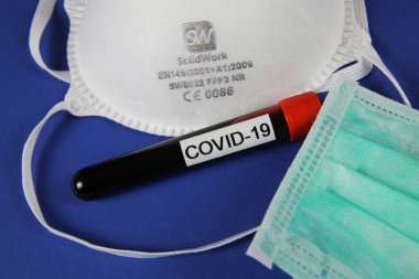 Viersen, Almanya - 28 Mart 2020: İzole CE sertifikalı koruyucu ffp2 ve yeşil cerrahi maske ile kan örneği tüp covid-19, mavi arkaplan