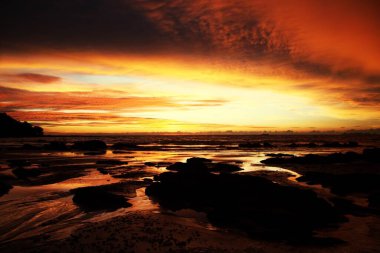 Ko Lanta, Tayland 'daki tropikal bir adada gün batımında sarı ve kırmızı ışıkta asılı duran derin fırtına bulutları ve ıslak çamur.