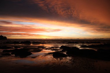 Ko Lanta, Tayland 'daki tropikal bir adada gün batımında sarı ve kırmızı ışıkta asılı duran derin fırtına bulutları ve ıslak çamur.