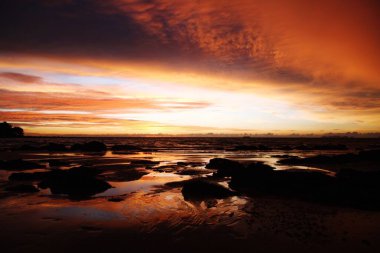 Ko Lanta, Tayland 'daki tropikal bir adada gün batımında sarı ve kırmızı ışıkta asılı duran derin fırtına bulutları ve ıslak çamur.