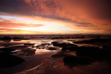Ko Lanta, Tayland 'daki tropikal bir adada gün batımında sarı ve kırmızı ışıkta asılı duran derin fırtına bulutları ve ıslak çamur.