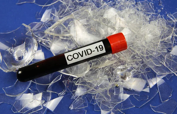 Health care system collapse and economic crisis concept: isolated blood sample vial with word covid-19 on pile broken glass shards (focus on vial)