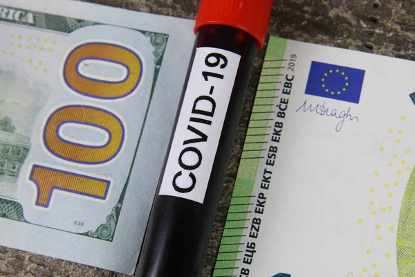 Covid-19 blood sample vial between 100 dollar us bank note and euro paper money bill