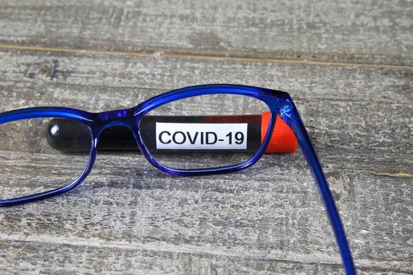 Research and learning about corona virus crisis concept: View through eyeglasses on blood sample vial with text covid-19