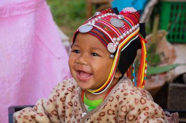 MAE SALONG, THAILAND 17 ARALIK. 2017: Akha Hill kabilesinden mutlu bir bebeğin portresi, geleneksel şapka takan bir alışveriş kutusunda