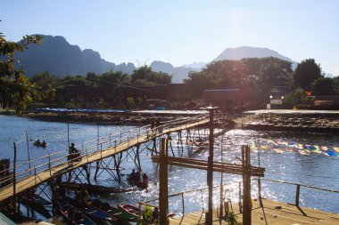 Akşam güneşinin alacakaranlığında nehrin üzerinde dar bir bambu köprüsü Vang Vieng, Laos
