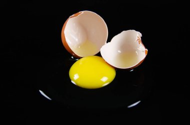 Koyu kahverengi yumurta kabuğunu, çiğ sarı yalk ve parlak siyah arkaplanı yansıtan sümüksü yumurta beyazıyla kapatın.