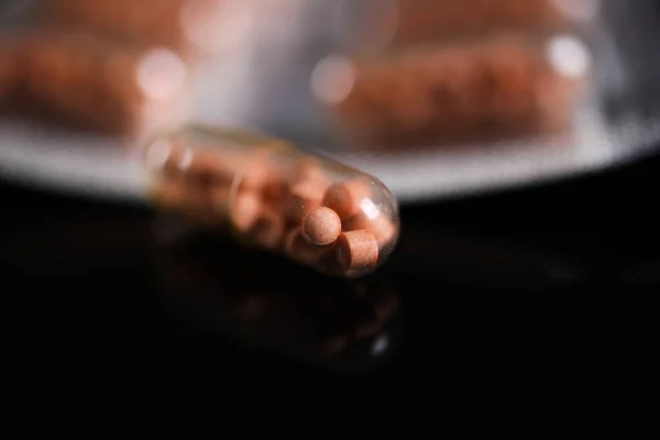 Makro close up of capsule pills in silver blister package and one isolated capsule with black reflecting background. Transparent shell showing pearls like ingredients.