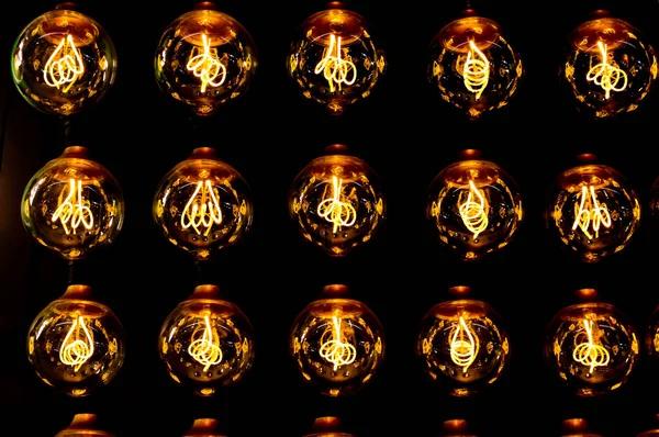 輝くフィラメントと黒の背景を持つ行にレトロな古典的な電球を輝く黄色の金の分離グループ — ストック写真
