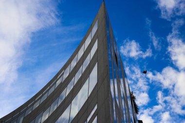 Modern gökdelenin keskin kenarına alçak açılı bir bakış açısı var. Mavi gökyüzüne karşı kıvrımlı bir cephe ve bulutlar - Duesseldorf, Almanya