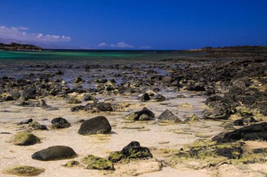El Cotillo, Kuzey Fuerteventura: Derin mavi gökyüzüne karşı La Concha sahilinin turkuaz gölünde sığ sularda, parlak dağınık taşlı plaja bakın
