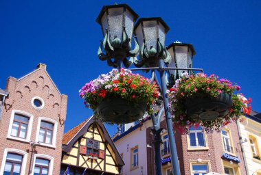 Oturma odası, Güney Bölgesi - 29 Haziran. 2019: Ortaçağ evlerinin arka planında mavi gökyüzüne karşı çiçek sepetleriyle süslenmiş sokak lambalarının alçak açısı